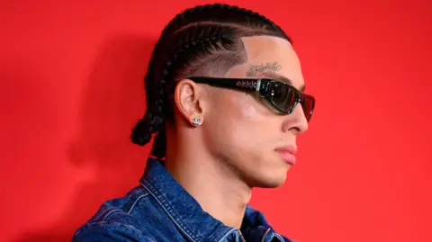 Getty Images Central Cee pictured at the GQ awards in 2024. He wears a denim jacket and sunglasses, the tattoo 'family' above his right eye visible in the side-profile shot. He's pictured against a red backdrop.