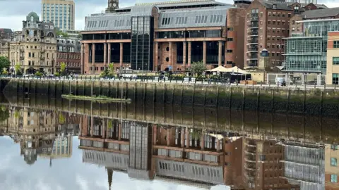 BBC The imposing court building made of red bricks and large dark windows reflected in the river. 