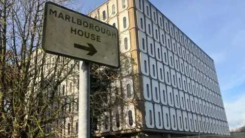 BBC A sign saying Marlborough House in front of a square grey building with rows of thin oval shaped windows.