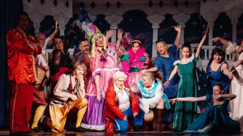 Lauren Moses A group of people wearing pantomime costumes stood on stage.