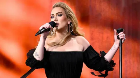 Getty Images Adele wearing a black dress and singing into a microphone.