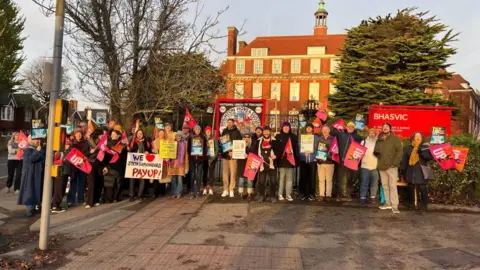 George Carden/BBC Dozens of teachers stage a protest outside a red brick school building. 