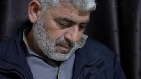BBC Tearful old man looks down. Tear shows on his cheek.