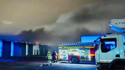 Aberdeen Harbour Tours Firefighters at scene of major blaze, fire engine next to crews, and flames and smoke coming from a building.