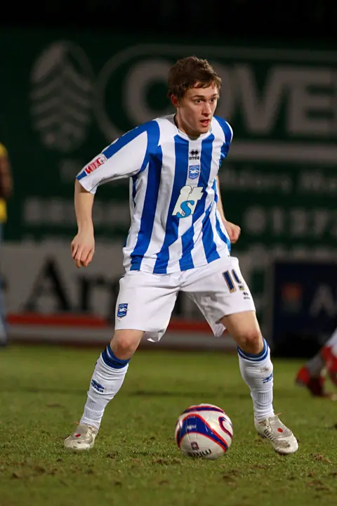 Paul Hazlewood/BHAFC Jake dribbling with the ball at the Withdean, Brighton's then-home stadium, in 2009. He is wearing the club's blue and white home kit which has white socks and shorts. The ball is blue, red and white.