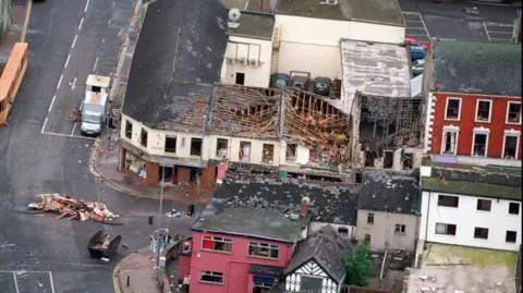 Press Association/MOD An aerial view of the 1998 Omagh bomb scene supplied by the Ministry of Defence. It shows several badly damaged buildings at the corner of Market Street. Some of the roofs have collapsed and there are piles of broken furniture and wood in the middle of the junction.