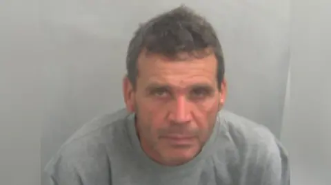 Essex Police Calogero Ricotta is in custody wearing a grey jumper. He has greying hair and is unshaven.