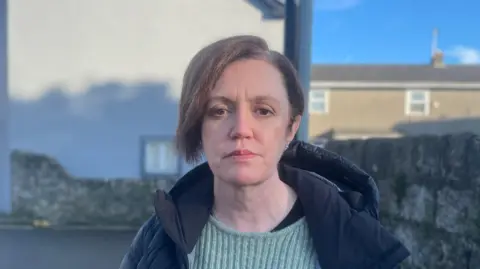 Contributor picture Jo Whitfield looking at the camera with a straight face. She has dark chin-length hair and is wearing a black down jacket with a light green jumper underneath.