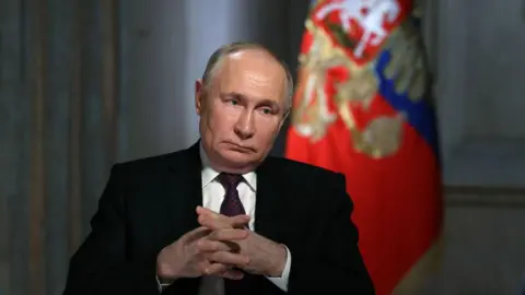 Getty Images Vladimir Putin staring with his hands crossed.