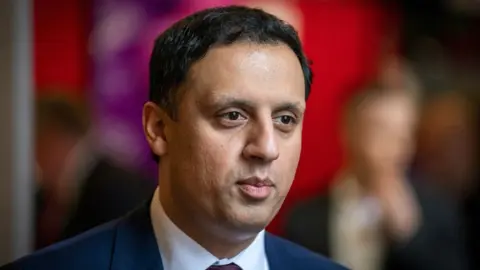 PA Media Anas Sarwar, who has dark hair, photographed in a close-up shot. He is visible from the shoulders up, and is wearing a navy suit and white shirt. 