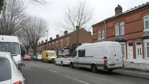 BBC A street scene with vehicles parked either side of a road which is lined with terraced houses.