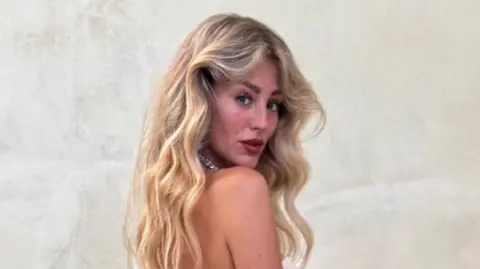 Charlene Morrisey A woman with blonde wavy hair looks at the camera over her shoulder.