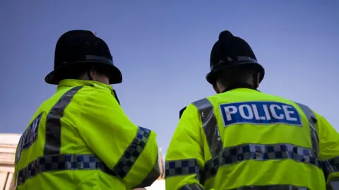 andrewmedina/Getty Creative Shot of the back of a couple of British Police officer's reflective yellow high vis jackets with the word police written across the back. 