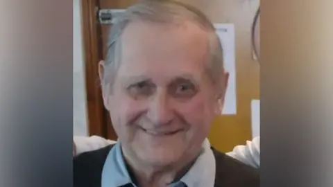POLICE SCOTLAND William Brown looking directly at the camera. He has grey hair. He is smiling. He is wearing a blue shirt, the collar of which can be seen, under a black jumper.