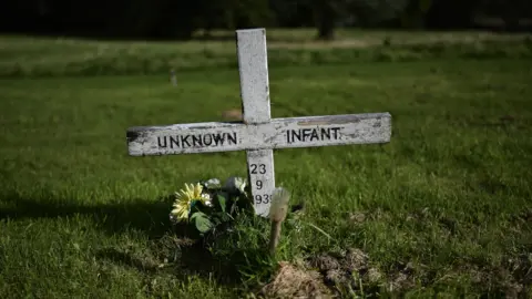 Getty Images A white cross on a green lawn that reads: 'unknown infant, 23 9 1939"
