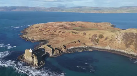 Mowi An aerial view of the island of Sanda and its lighthouse. The Kintyre peninsula is across the sea from it.