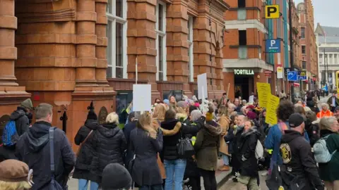 JohnLawrence Protesters gather on a street with placards and signs outside the red bricked entrance to the Greater Manchester Combined Authority's Oxford Street office.