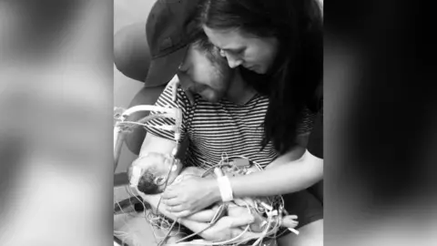 Ryan Parker/Emmie Studencki A black and white image of Quinn Parker, who has a number of wires and tubes going into this nose and mouth, being held.