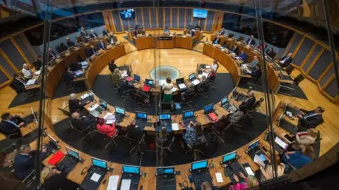 Senedd Cymru A general view of the Senedd debating chamber full of politicians seen from above.