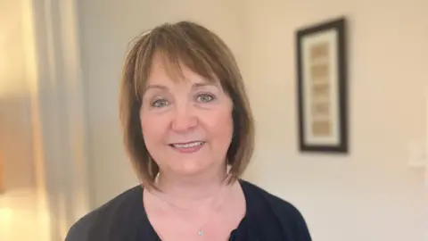 Margie Button. She has short brown hair with a fringe, wearing a black top and necklace. She is smiling at the camera.