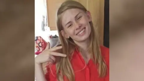 Family handout Rhianan Rudd smiling for the camera. She has blonde hair and is wearing a red shirt.