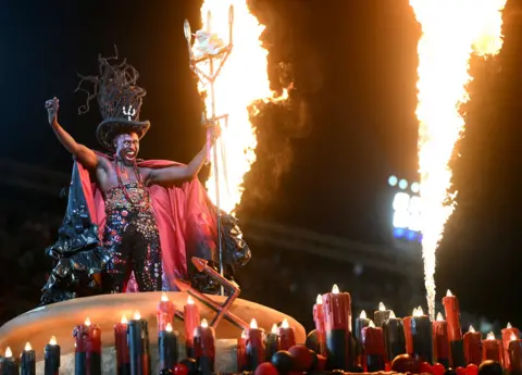 Mauro Pimental / AFP A reveler of the Beija-Flor samba school performs dressed as a devil. He is is gesturing and is surrounded by jets of flame.