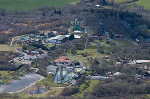 Getty Images An aerial view of Oakwood theme park. A number of large rollercoasters can be seen spread across the park, with grass and trees in between the attractions. A large white building can be seen at the back of the park.