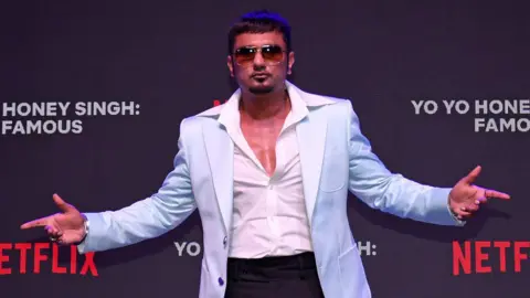 Getty Images Indian music producer and actor Hirdesh Singh (professionally known as Yo Yo Honey Singh) wearing a light blue blazer with a white shirt and black trousers with oversized sunglasses poses for a photo at an event to unveil his upcoming documentary 'Yo Yo Honey Singh : Famous' on Netflix in Mumbai.