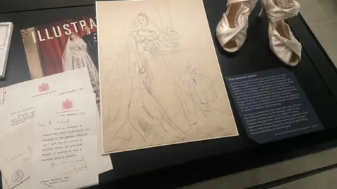 Correspondence between Queen Elizabeth II and Norman Hartnell alongside sketches for her wedding dress and an early mock-up of her wedding shoes.