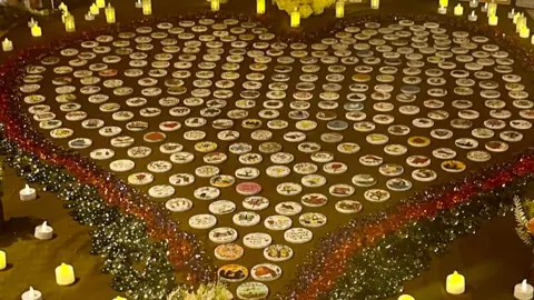 A large heart encompasses loads of white badges, all with different designs. The heart has candles around the outside of it and is green, orange and purple in colour.
