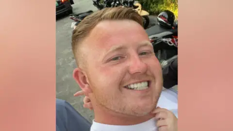 Supplied A headshot selfie of Tommy Hunter, standing in front of motorcycles