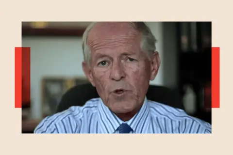 . John Smyth speaking to camera, his lips pursed