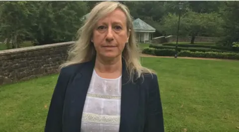 BBC Anna-Louise Marsh-Rees in black jacket which is over a white lace top. She is stood in a garden and is looking at the camera.