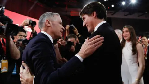 Reuters Mark Carney and Justin Trudeau embrace as a crowd of photographers take photos and Trudeau's daughter, who had introduced her father at the Liberal Party event, watch on.
