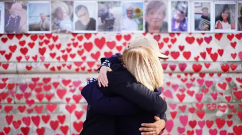 PA Media People hugging as they attend a ceremony marking the fifth anniversary of the Covid-19 pandemic at the National Covid Memorial Wall in London.