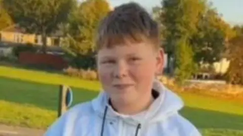 Heather Lane Alfie Lewis looks at the camera. He has short hair and is wearing a white hooded top