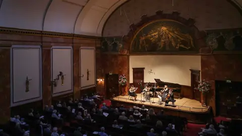 Getty Images A wide view of Wigmore Hall showing the audience and a string quartet lit up on the stage under ornate ceiling decoration