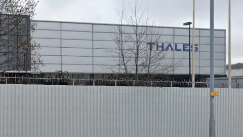 Google THALES title is top right in dark blue. The building is made up of reflective windows and has high walled security.