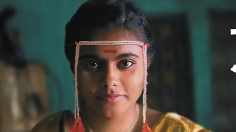 Courtesy: Sthal A still from Sthal: A Match shows the lead character played by Nandini Chikte sitting on a wooden stool