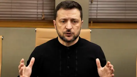 Reuters Volodymyr Zelensky sits in a black top with his hands outstretched