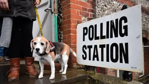 Getty Images A voter wearing brown boots and a long grey cardigan leaves a polling station in Brighton with a small brown dog on a yellow leash.