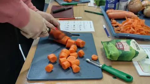 London Borough of Sutton Close up photo of a female hand cutting a carrot on a chopping board