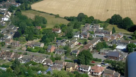 Thomas Nugent/Geograph Breachwood Green from the air, showing a settlement of mainly two-storey houses in brick and stone. There are trees between the houses and fields in the background.