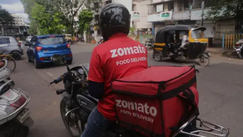 Getty Images A delivery worker of Zomato, an Indian food-delivery company, waits to pick up an order from a restaurant in Mumbai, India, 02 October, 2022. (Photo by Niharika Kulkarni/NurPhoto via Getty Images)