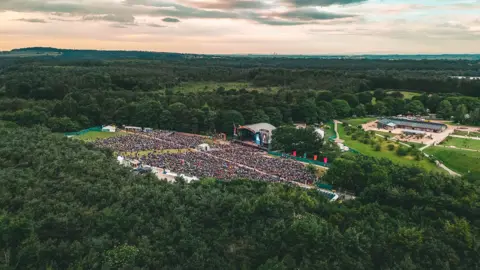 Forest Live An aerial view of a crowd of people gathered in front of a stage in the middle of a forest.