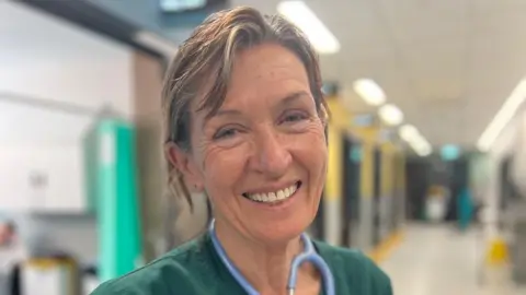 Great Western Hospital NHS Foundation Trust Dr Sian Thomas smiles at the camera for a portrait shot, she wears green scrubs and you can see a stethoscope hangs round her neck.