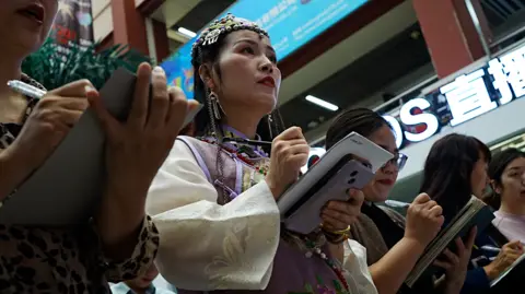 BBC/ Xiqing Wang Women stand in a line with notebooks and phones
