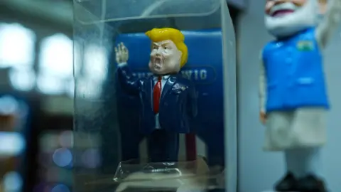 BBC/ Xiqing Wang A toy Trump in a blue jacket and red tie in a glass case in a stall in Yiwu.
