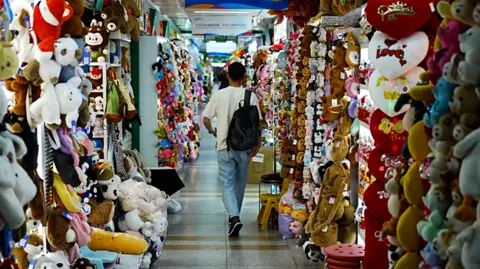 BBC/ Xiqing Wang A man walks down a hall lined with toys hanging up