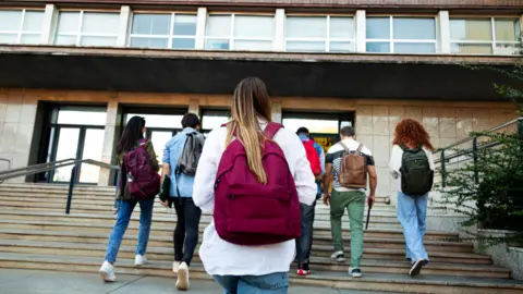 Getty Images A group of students with their backs to the camera walking up the stairs into a campus building 